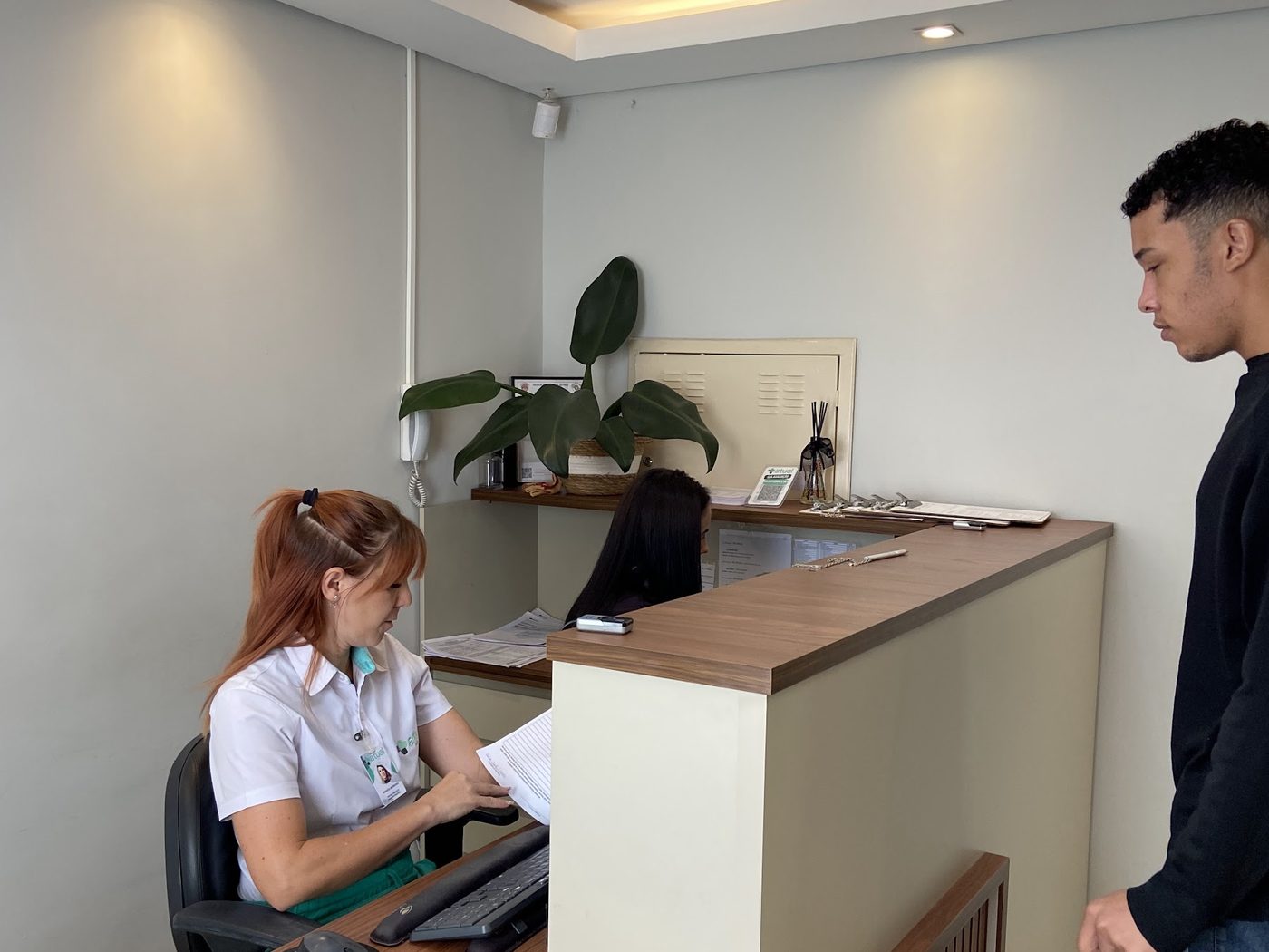Recepcionista da Atual Medicina atendendo um paciente no balcão da recepção